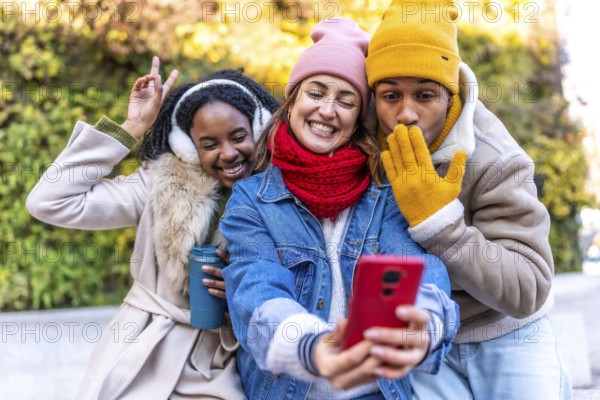 Group of cheerful multi ethnic friends taking a selfie with a smartphone in a city park during wintertime