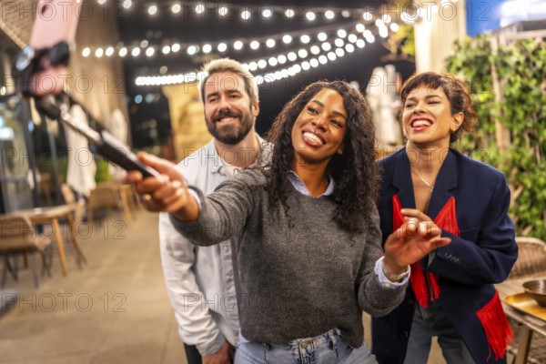 Latin woman streaming online during night party with multi-ethnic friends in the roof terrace of a bar