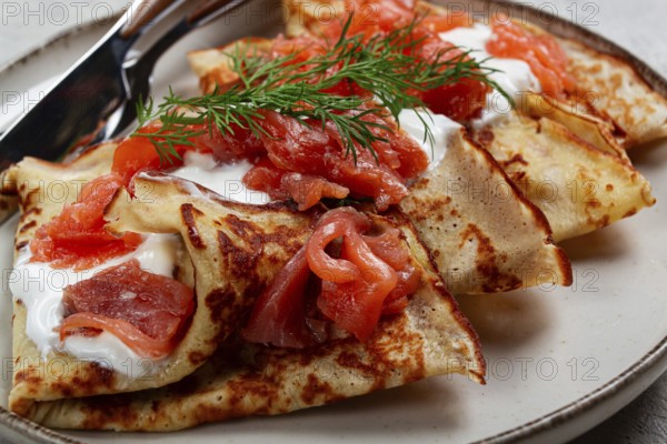 Delicious pancakes with salmon and sour cream, breakfast, on a plate, rustic style, with cutlery