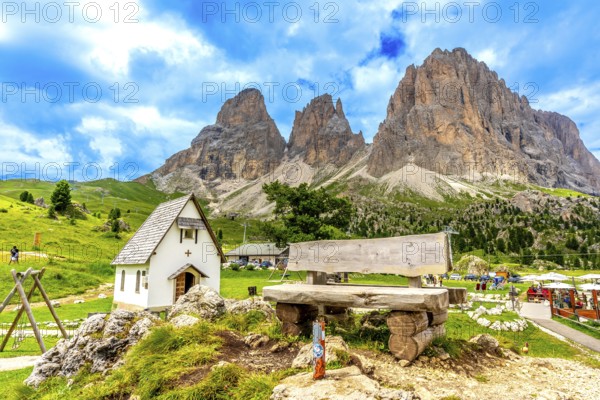 Breathtaking summer view of the majestic sassolungo mountain at sella pass, featuring a wooden bench and a small church in the dolomites, italy
