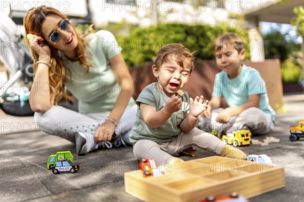 Young caucasian mother with baby and son playing sitting in a park