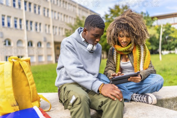 Multiethnic young students studying together using digital tablet sitting outside the university campus in a sunny day of autumn
