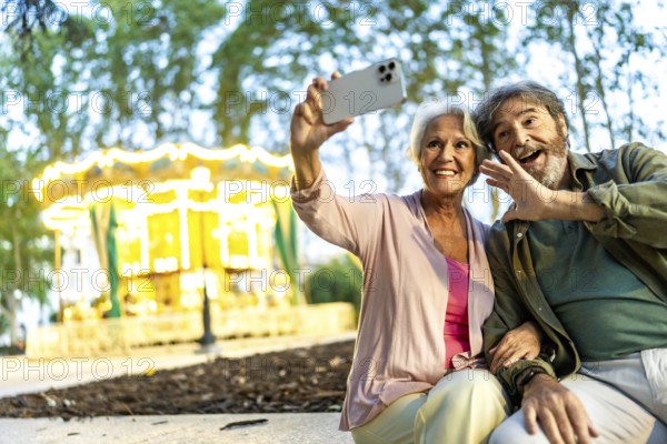 Senior couple waving while taking selfie sitting on bench in the city fair