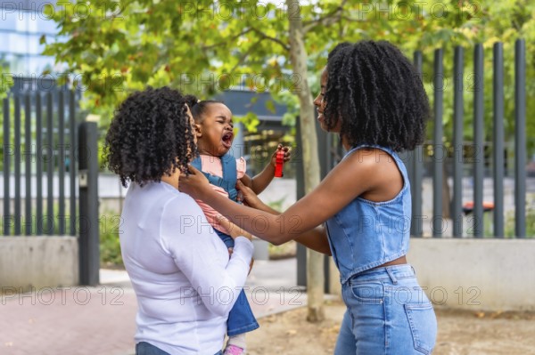 African schoolgirl crying in the park next to her mother and granny that is carrying her