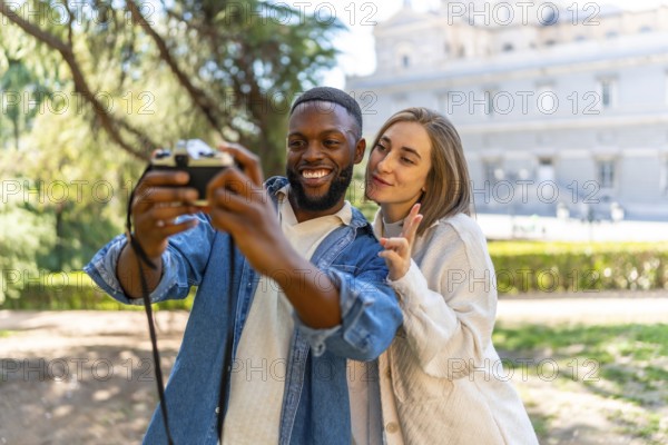 Cute multi-ethnic couple taking selfie with digital camera in a city view point