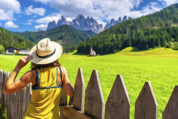 Female tourist wearing a straw hat admiring the stunning view of the odle mountains and st. Magdalena church in val di funes
