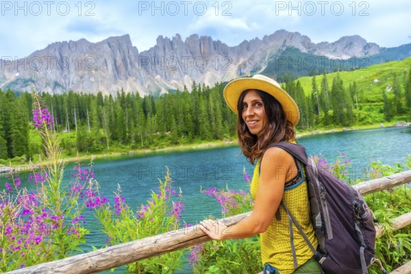 Female tourist with backpack and straw hat enjoying the landscape of lake carezza and latemar mountain in the dolomites, italian alps