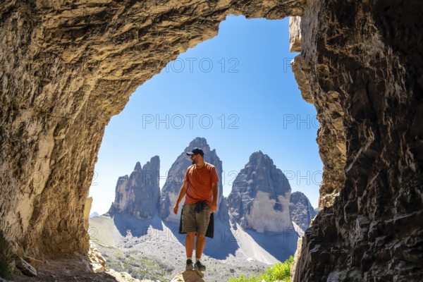 Hiker enjoying the scenic view of tre cime di lavaredo, a symbol of the dolomites, from inside a mountain Tre Cime Cave during a summer hike