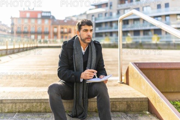 Man in elegant winter clothes writing notes sitting on an urban space