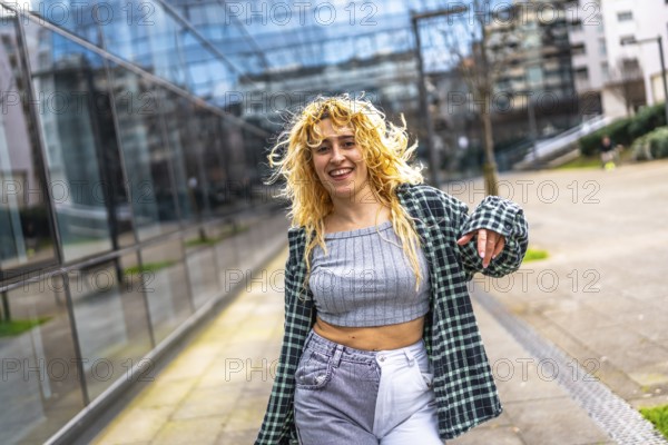 Carefree young woman with curly blonde hair enjoying dancing to urban music in a city street, expressing freedom and joy