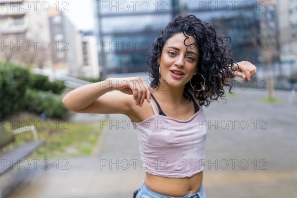 Curly haired woman dancing outside, performing a modern dance routine in an urban environment