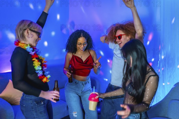 Cheerful multi ethnic friends dancing together and enjoying drinks at a home disco party with blue and pink lighting