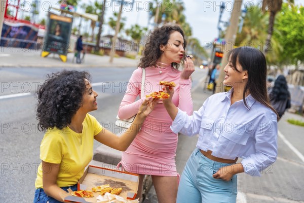 Three cool diverse women sharing take away pizza in the street