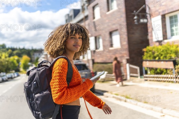 Side view of a latin beauty female student with curly hair walking while using phone in the city