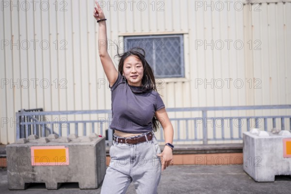 Asian young woman pointing to the sky dancing k-pop urban dance outside an industrial building in the city