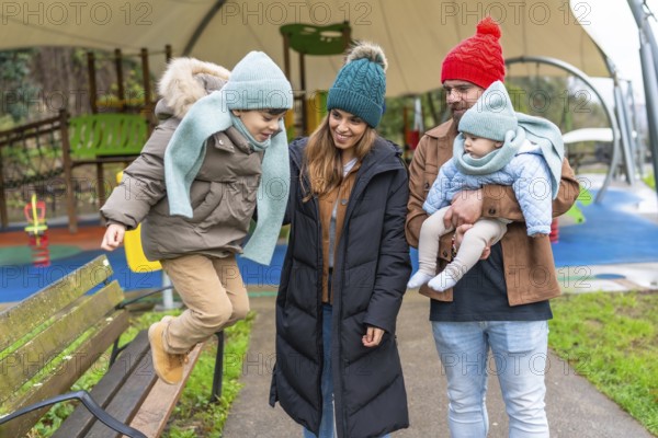 Smiling family enjoying a joyful winter day at the playground, with children happily jumping on a bench and playing together