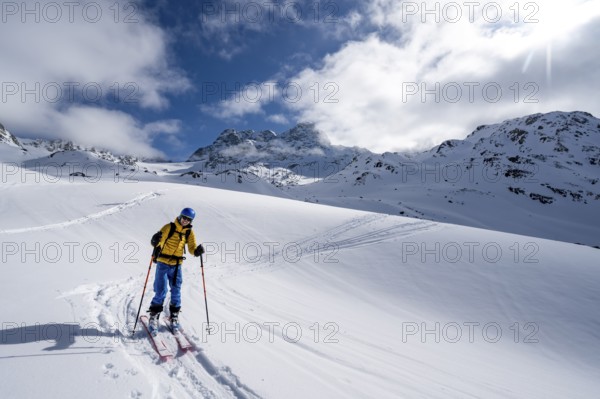 Ski tourer ascending through a picturesque snow-covered mountain landscape with views of mountain peaks, ascent to the summit of Kesch Pitschen, Bündner Haute Route ski tour, Albula Alps, Rhaetian Alps, Grisons, Eastern Switzerland, Switzerland, Europe