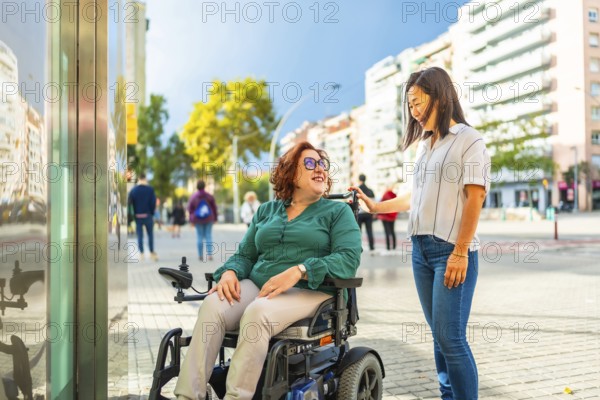 Disabled woman in wheelchair and chinese caregiver waiting at metro elevator in the city during sunny day