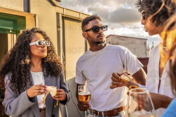Multi-ethnic modern friends talking in a rooftop while drinking wine and eating snacks