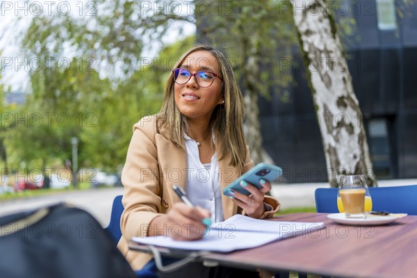 Latin businesswoman writing notes during coffee break outdoors in an outside terrace of a cafeteria