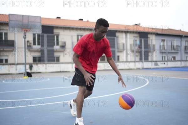 Full length photo of a sportive young african man dribbling at a basketball court