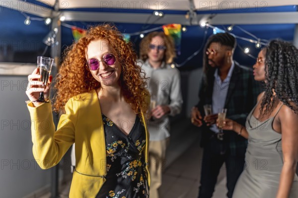 Happy redhead beauty millennial woman toasting at camera at night roof party with multi-ethnic friends