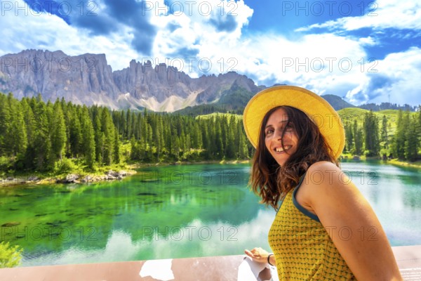 Tourist admiring the stunning emerald waters of lake carezza, with the latemar mountain range in the background, on a sunny summer day in the italian dolomites