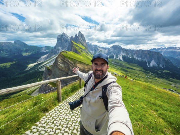 Photographer with backpack and camera taking a selfie with outstretched arm with the odle di eores mountain group in the background
