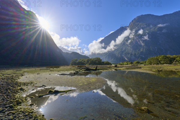 Dramatic sunbeams over mountains with clouds and water reflection, summer, Milford Sound, Te Anau, Fiordland National Park, South Island, New Zealand, Oceania