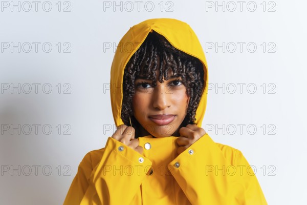 Studio portrait of a young woman with curly hair wearing a yellow raincoat and pulling the hood strings
