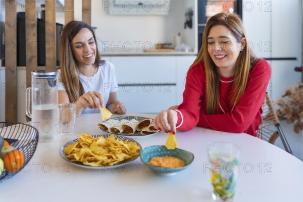 Two cheerful women enjoying a meal of quesadillas, nachos and sauce, creating a cozy and joyful atmosphere