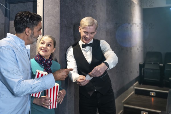 Couple holding popcorn buckets showing their tickets to the usher before entering the movie theater