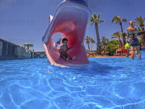 Young boy enjoying summer vacation sliding down a waterslide shaped like a monster's mouth into a refreshing blue pool