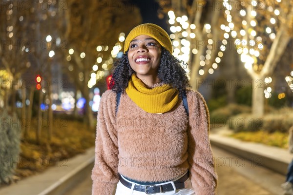 Happy young woman wearing winter clothes walking down a decorated street enjoying christmas lights