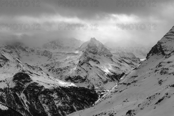 Dark clouds and wafts of mist surround the snow-covered summit of Mount Le Besso, view from the Sorebois summit station, black and white photo, Val d'Anniviers, Valais Alps, Canton Valais, Switzerland, Europe