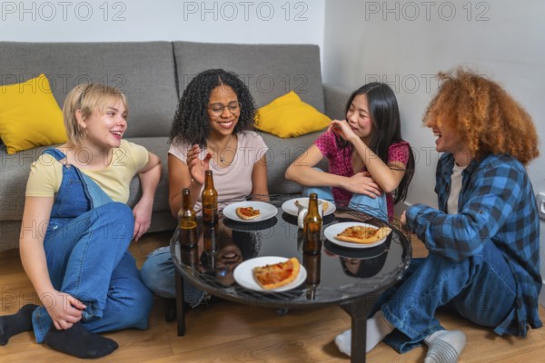 Group of young multi ethnic friends laughing and eating pizza and drinking beer, sitting around a table in a living room