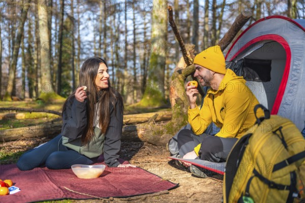Hikers enjoying a healthy snack of fruit during a camping trip in a sunny forest, promoting a connection with nature and a healthy lifestyle