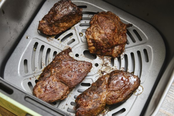 Juicy beef steaks rest inside an air fryer basket after cooking. The perfectly seared meat showcases a rich brown crust, enticing anyone for a satisfying meal