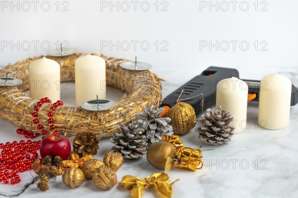 Craft scene with Advent wreath, white candles, decoration material and a glue gun on a marble surface