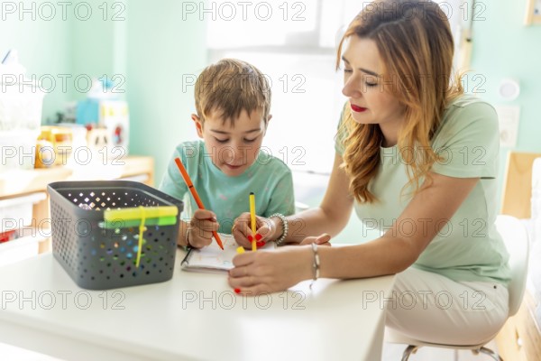 Happy and tender scene of a mother and school boy coloring at home together