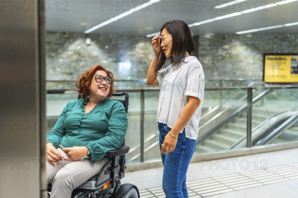 Smiling caucasian adult disabled woman and asian female friend talking waiting for subway elevator