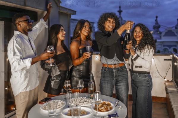 Happy man opening a champagne bottle celebrating night party in a rooftop with multiracial friends