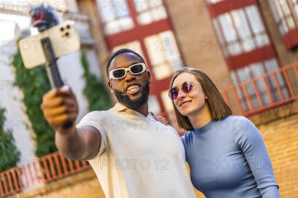 Smiling multiracial cool modern couple vlogging through mobile phone in the city street