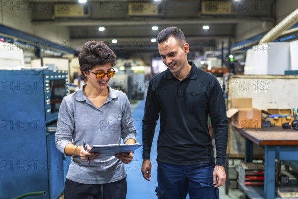 Woman manager and male worker walking checking stock inventory with clipboard and discuss talking together in manufacturing factory