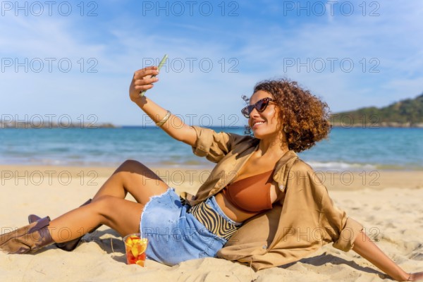 Sensual arab modern woman wearing bikini and denim shorts taking selfie sunbathing on the beach