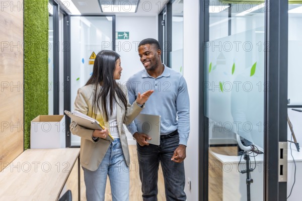 Two managers are walking through a modern coworking office, holding laptops and discussing work