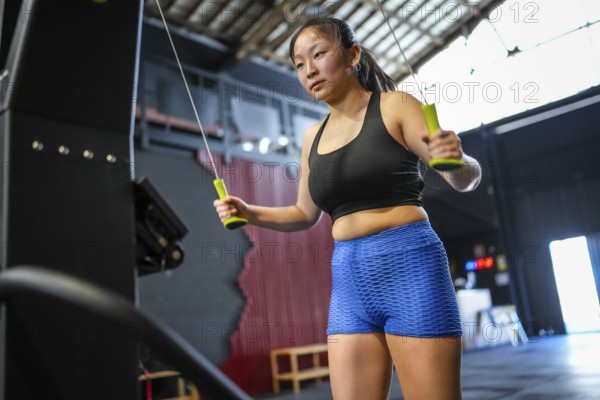 Low angle view three quarter length photo of an asian woman training using lat machine to pull weights