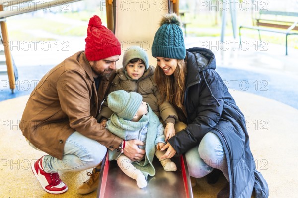 Parents assisting their children as they joyfully slide down a playground slide, embracing the fun and laughter of winter outdoors