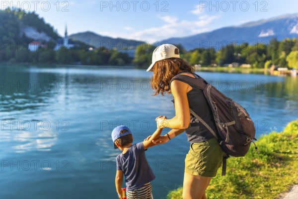 Mother and son holding hands, enjoying summer vacation by the turquoise water of lake bled, with the iconic church on bled island in the background