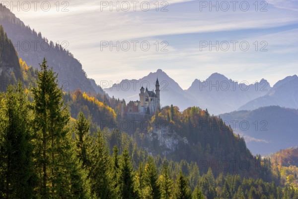 Panoramic view of Neuschwanstein Castle in front of wide mountain ranges and dense autumn forest, Neuschwanstein, Schwangau, Ostallgäu, Allgäu, Swabia, Upper Bavaria, Bavaria, Germany, Europe